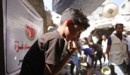 A Palestinian boy licks his fingers as he scrapes the pot for a portion of food at a food distribution point in Gaza City on June 27, 2025. (Photo by Bashar Taleb / AFP)