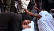 Palestinians mourn over the shrouded bodies of people killed during a reported Israeli strike on a humanitarian aid distribution warehouse in the Sabra neighbourhood in Gaza City, in the central Gaza Strip, on the grounds of Al-Ahli Arab hospital, also known as the Baptist hospital on June 30, 2025. (Photo by Omar AL-QATTAA / AFP)