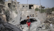 A Palestinian boy checks the wreckage of a car at the rubble of a residential house in Deir el-Balah in the central Gaza Strip on July 1, 2025. (Photo by Eyad BABA / AFP)
