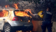 A police officer tries to put off the fire in a car during a wildfire, in L'Estaque district of Marseille, southern France on July 8, 2025. Photo by Clement MAHOUDEAU / AFP.
