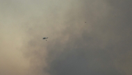 A firefighting helicopter flies through smoke from a wildfire which started in the municipality of Mentrida near Toledo, as seen from Arroyomolinos, outside Madrid on July 17, 2025. Photo by JAVIER SORIANO / AFP.
