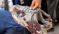 A person holds the bloodied shoes of young man who was killed by gunfire while waiting for aid trucks entering the northern Gaza Strip through the Zikim crossing, as people gather around the body at the Shifa Hospital in Gaza City on July 27, 2025. (Photo by Omar AL-QATTAA / AFP)