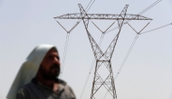 An Iraqi man stands under an electricity transmission tower south of Hilla city on August 10, 2025, amidst rising temperatures, chronic water shortages and power cuts. (Photo by AHMAD AL-RUBAYE / AFP)
