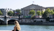 A woman walks past the Seine River and the French National Assembly, the lower House of Parliament, in Paris on August 11, 2025, amid a heatwave in Europe. (Photo by Martin LELIEVRE / AFP)