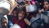 Palestinian women and children hold out their empty pots in front of a charity kitchen in Khan Yunis in the southern Gaza Strip on August 21, 2025. Photo by AFP