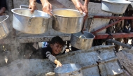 A Palestinian boy extends an empty pot in front of a charity kitchen to receive cooked rice, in Gaza City on August 23, 2025. Photo by Omar AL-QATTAA / AFP.
