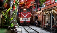 This photo taken on August 18, 2025 shows a train as it passes along a railway track between cafe terraces in central Hanoi. (Photo by Nhac Nguyen / AFP)