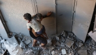 Graphic content / A Palestinian man carries an injured child from inside a building that was targeted in an Israeli strike in the Al-Rimal neighbourhood of Gaza City on August 30, 2025. (Photo by Omar Al-Qattaa / AFP)