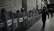 Mexican riot police officers take cover behind their shields during a protest over the 11th anniversary of the disappearance of 43 students from Ayotzinapa in Mexico City on September 26, 2025. (Photo by Carl De Souza / AFP)