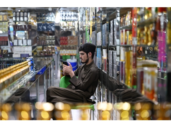 An Afghan vendor selling perfume and body sprays, uses his mobile phone as he sits at his shop in Kabul on October 1, 2025.  (Photo by Wakil Kohsar / AFP)
