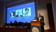 Nobel Committee Secretary General Thomas Perlmann (R) addresses journalists in front of a screen displaying the portraits of (L-R) Mary E Brunkow, Fred Ramsdell and Shimon Sakaguchi during a press conference. (Photo by Jonathan Nackstrand / AFP)