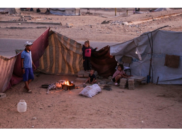 Palestinians sit by the fire in their makeshift shelter in Khan Yunis, in the southern Gaza Strip on October 25, 2025. (Photo by Bashar Taleb / AFP)
