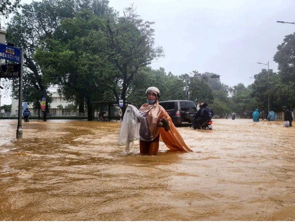 A woman wearing a raincoat wades through a flooded street in Hue on October 28, 2025. Photo by AFP