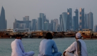 People sit along the corniche facing traditional dhow boats anchored in front of the Doha skyline on October 29, 2025. (Photo by Karim Jaafar / AFP)