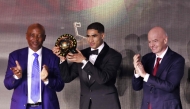 Paris Saint-Germain's Moroccan defender Achraf Hakimi (C) holds his Africa Player of the Year award next to CAF President Patrice Motsepe (L) and FIFA President Gianni Infantino (R) during the 2025 Confederation of African Football (CAF) Awards in Sale, Morocco on November 19, 2025. Photo by Abdel Majid Bziouat / AFP