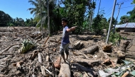 A man walks across mud and debris in a flood affected area in Meureudu, Pidie Jaya district in Indonesia's Aceh province on November 30, 2025. (Photo by Chaideer Mahyuddin / AFP)