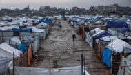Men walk along a muddy alley at a makeshift camp sheltering displaced Palestinians after heavy rains in the Zeitoun neighbourhood of Gaza City on December 11, 2025. (Photo by Omar AL-QATTAA / AFP)
