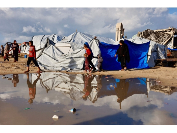 Displaced Palestinians walk past a large pool of rain water accumulated near tent shelters as the region experiences rain and cold winter conditions, in Gaza City on December 28, 2025. Photo by Omar AL-QATTAA / AFP