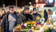Mourners gather in front of flowers and candles laid near the site where a fire ripped through a crowded establishment during New Year's Eve celebrations in the Alpine ski resort town of Crans-Montana on January 1, 2026. Photo by MAXIME SCHMID / AFP