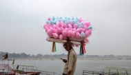 A cotton candy vendor uses his mobile phone as he waits for customers along the banks of the river Ganges in Varanasi on January 29, 2026. (Photo by Niharika KULKARNI / AFP)