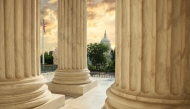 US Capitol building viewed between columns of the Supreme Court at sunset.