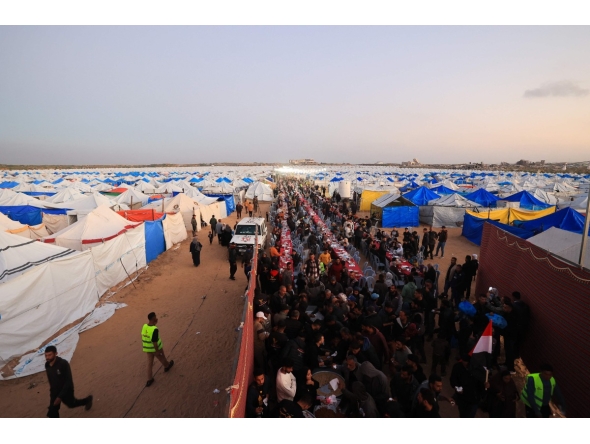 Displaced Palestinian families sit at communal long tables as they gather to break the dawn-to-dusk Ramadan fast during Iftar, in the al-Zahara neighborhood, north of the Nuseirat refugee camp in the central of Gaza Strip on February 21, 2026. (Photo by Eyad Baba / AFP)
