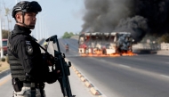 A member of the Prosecutor's Office stands guard near a burning bus at one of the main avenues after it was set on fire by organised crime groups in response to an operation in Jalisco to arrest a high-priority security target in Zapopan, state of Jalisco, Mexico, on February 22, 2026. (Photo by Ulises Ruiz / AFP)