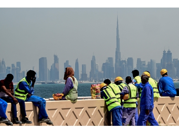 (Files) Workers sit on a wall against the backdrop of the Dubai city skyline on March 11, 2026. (Photo by Giuseppe Cacace / AFP)