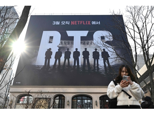 A woman uses her smartphone in front of a billboard promoting a comeback concert of K-pop boy group BTS at Gwanghwamun Square in Seoul on March 17, 2026. (Photo by Jung Yeon-je / AFP)
 