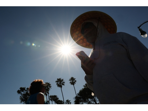 A person wears a hat for shade under the morning sun while walking along The Strand in Redondo Beach, California on March 20, 2026, during a heat wave. (Photo by Patrick T. Fallon / AFP)