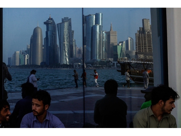 People sit with the reflection of the Doha skyline along the Doha Corniche in Doha on March 21, 2026. Photo by AFP