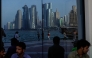People sit with the reflection of the Doha skyline along the Doha Corniche, in Doha on March 21, 2026. Photo by AFP
