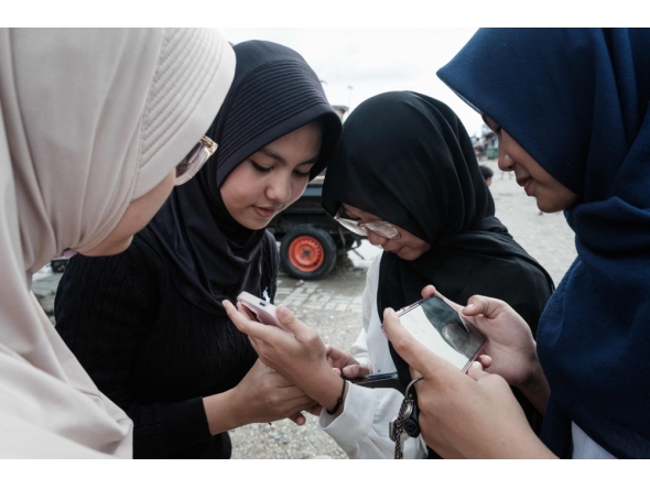15-year-old girls use their smartphones on a street in Jakarta on March 26, 2026. (Photo by Yasuyoshi Chiba / AFP) 