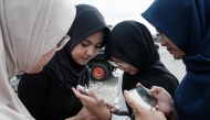 15-year-old girls use their smartphones on a street in Jakarta on March 26, 2026. (Photo by Yasuyoshi Chiba / AFP) 