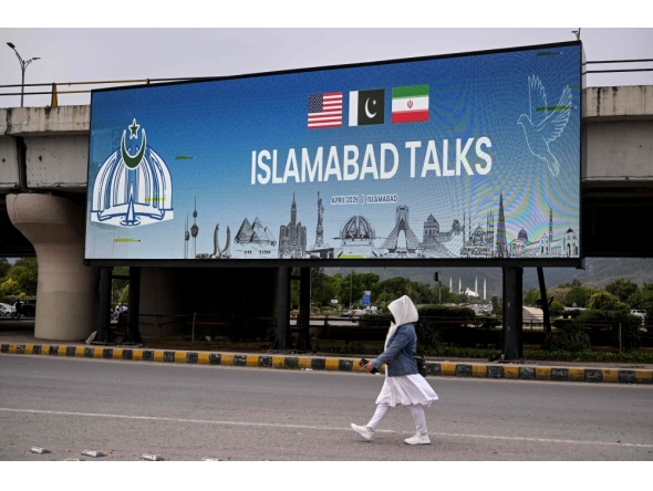 A woman walks past a digital screen displaying news of US-Iran peace talks along a road in Islamabad on April 10, 2026. (Photo by Farooq Naeem / AFP)