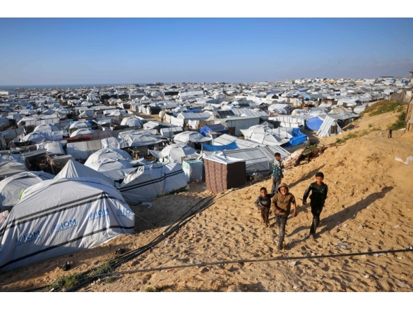 Boys walk past the tents at a makeshift camp for displaced Palestinians in Khan Yunis, in the southern Gaza Strip on April 10, 2026. (Photo by Bashar Taleb / AFP)