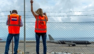 Representatives from the Netherlands embassy wave as a plane bound for the Netherlands carrying passengers evacuated from the Dutch-flagged hantavirus-stricken cruise ship MV Hondius prepares to take off from the Tenerife Sur-Reina Sofia airport on the island of Tenerife in Spain's Canary Islands on May 10, 2026. (Photo by Antonio Sempere / AFP)