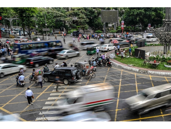This photograph taken on May 14, 2026 shows commuters waiting to cross a road amid traffic in Dhaka. Photo by Munir UZ ZAMAN / AFP