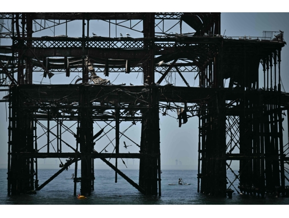 A paddleboarder is seen between the stanchions of the derelict West Pier off the beach in Brighton, on the south coast of England on May 25, 2026, as Monday is expected to be the hottest bank holiday.(Photo by Ben Stansaal / AFP)
 