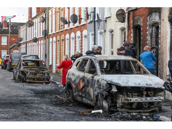 Residents and members of the media look at burnt-out cars and homes after demonstrations turned violent the night before, in eastern Belfast, Northern Ireland, on June 10, 2026. Photo by Paul Faith / AFP