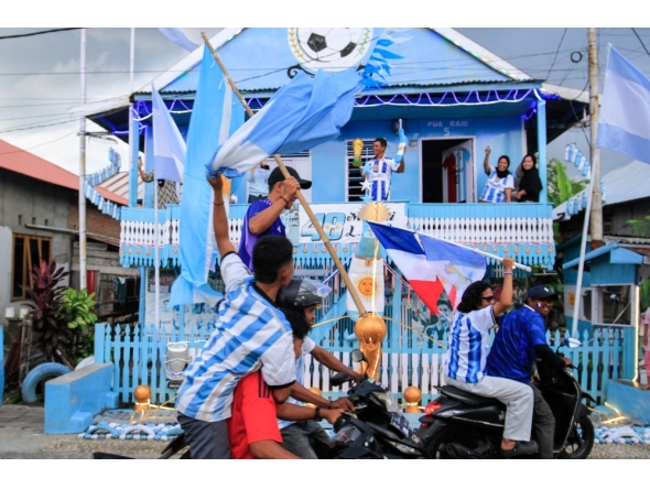 Argentina fan and fisherman Muhammad Yusuf (back C) holds a replica of the World Cup trophy as football fans pass his house, painted in the colours of the Argentine national team in Indonesia's West Sulawesi on June 11, 2026. (Photo by Muhammad Salim / AFP)