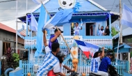 Argentina fan and fisherman Muhammad Yusuf (back C) holds a replica of the World Cup trophy as football fans pass his house, painted in the colours of the Argentine national team in Indonesia's West Sulawesi on June 11, 2026. (Photo by Muhammad Salim / AFP)