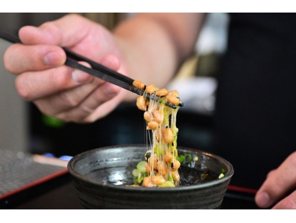 Kenji Suzuki, second-generation owner of Suehiro Japanese Restaurant in Los Angeles, California, lifting natto from a bowl with chopsticks. (Photo by Frederic J. Brown / AFP) 