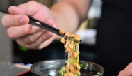 Kenji Suzuki, second-generation owner of Suehiro Japanese Restaurant in Los Angeles, California, lifting natto from a bowl with chopsticks. (Photo by Frederic J. Brown / AFP) 