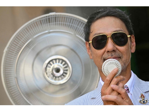 A guest holds a mini-fan to cool down before the Thom Browne collection show at Milan's Fashion Week Menswear Spring/Summer 2027, in Milan on June 22, 2026. (Photo by Stefano RELLANDINI / AFP)
