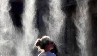 A woman cools off under a mist sprayer during the annual street music festival 'Fete de la Musique' while taking part in a heatwave in Bordeaux, southwestern France on June 21, 2026. (Photo by ROMAIN PERROCHEAU / AFP)
