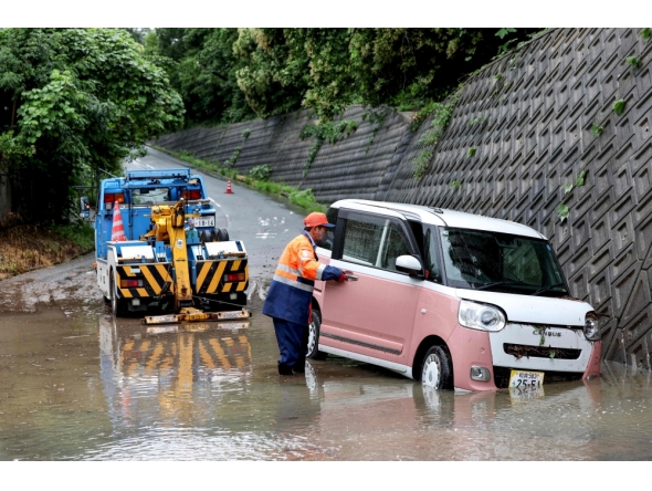 A tow lorry driver retrieves a partially submerged car after flooding in the town of Kashiwara, Osaka prefecture on June 26, 2026.  (Photo by Paul Miller/ AFP)