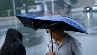 A man holding an umbrella walks along a road on a rainy day in Beijing on July 10, 2026. (Photo by WANG Zhao / AFP)