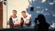 People pose for a photo with a mural of England footballers Jude Bellingham and Morgan Rogers, eating a portion of chips, created by artist Dion Kitson, on the wall of a fish and chip shop near Halesowen in central England, on July 14, 2026. (Photo by Oli Scarff / AFP)