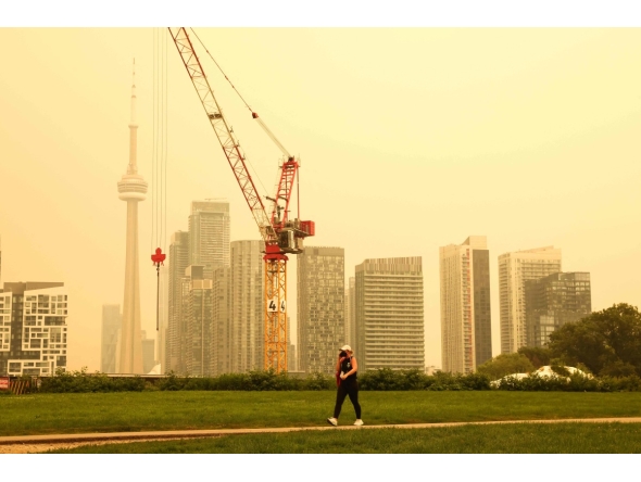 A person walks by the skyline of downtown Toronto, as smoke from forest fires in Northern Ontario causes poor air quality over the city, in Toronto, Ontario, Canada, Wednesday, July 15, 2026. (Photo by Cole BURSTON / AFP)
